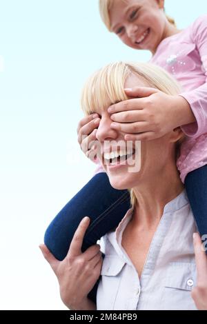 Ich führe dich an, mom. Ein kleines Mädchen, das die Augen seiner Mutter bedeckt, während sie auf den Schultern ihrer Mutter sitzt. Stockfoto