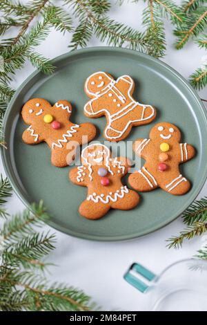 Lebkuchen-Kekse in Form eines Ingwermannes auf einem grünen Teller mit Kiefern als Dekoration. Traditionelles Weihnachtsdessert. Verspielt und ha Stockfoto