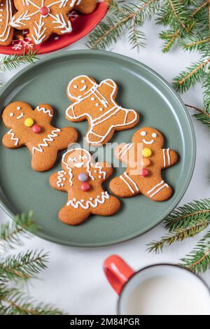 Lebkuchen-Kekse in Form eines Ingwermannes auf einem grünen Teller mit Kiefern als Dekoration. Traditionelles Weihnachtsdessert. Verspielt und ha Stockfoto