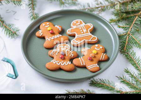 Lebkuchen-Kekse in Form eines Ingwermannes auf einem grünen Teller mit Kiefern als Dekoration. Traditionelles Weihnachtsdessert. Verspielt und ha Stockfoto