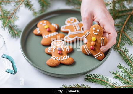 Lebkuchen-Kekse in Form eines Ingwermannes auf einem grünen Teller mit Kiefern als Dekoration. Traditionelles Weihnachtsdessert. Verspielt und ha Stockfoto