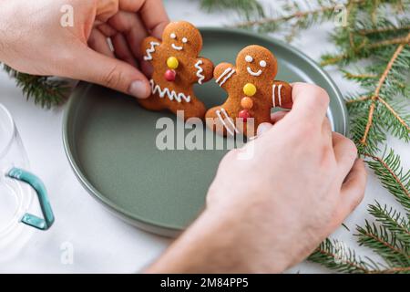 Lebkuchen-Kekse in Form eines Ingwermannes auf einem grünen Teller mit Kiefern als Dekoration. Traditionelles Weihnachtsdessert. Verspielt und ha Stockfoto