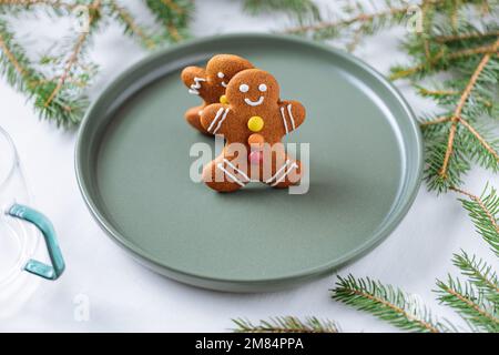 Lebkuchen-Kekse in Form eines Ingwermannes auf einem grünen Teller mit Kiefern als Dekoration. Traditionelles Weihnachtsdessert. Verspielt und ha Stockfoto