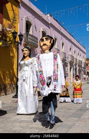 Riesenpuppen oder Monos de calenda und Frauen in traditionellen Kleidern, die sich für eine Hochzeitsparade in Oaxaca, Mexiko, einladen. Stockfoto