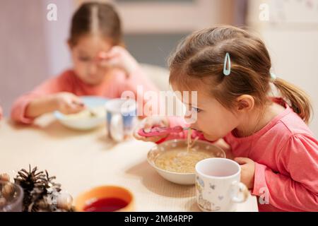 Zwei Schwestern essen zusammen in der Küche, das kleine Mädchen isst Bouillon. Stockfoto