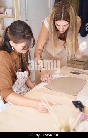 Freunde mit Schürzen in einer Töpferwerkstatt bereiten Ton vor, um Stücke zu kreieren. Handwerksklasse. Stockfoto