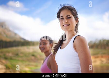 Joggen unter ländlicher Schönheit. Zwei junge Joggingweibchen lächeln fröhlich in die Kamera. Stockfoto