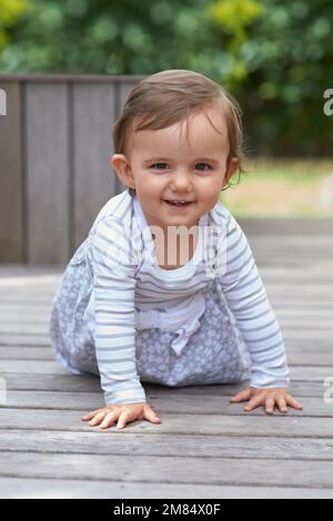 Sie ist eine neugierige kleine. Porträt eines süßen kleinen Babys, das auf einer Terrasse herumkrabbelt. Stockfoto