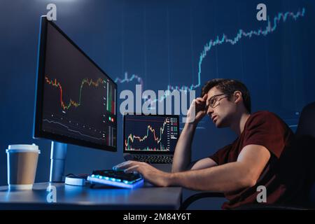 Krypto-Händler-Investor, der spät in der Nacht auf einen Computerbildschirm mit Kerzenleuchtendiagramm blickt und über die globalen Risiken des Online-Börsenmarkts nachdenkt, die durch die globale Rezession und den Verlust von Geld verärgert sind Stockfoto