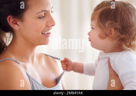 Einen süßen Moment teilen. Ein kleines Mädchen, das an ihrem Muttertop zieht. Stockfoto