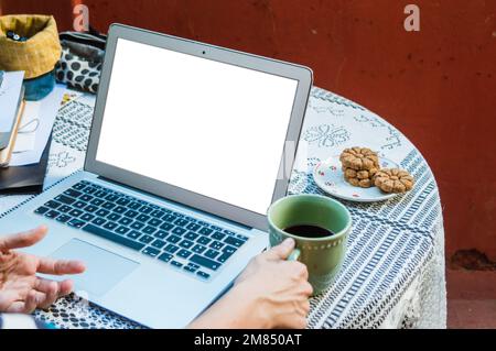 Offener Laptop auf Tisch mit leerem Bildschirm, weiße Handtasse für Frauen mit Kaffee auf Terrassentisch, Business-Konzept, Kopierbereich. Stockfoto