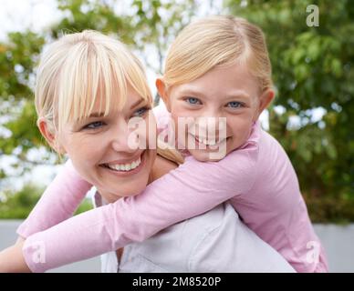 Diese besondere Verbindung zwischen Mutter und Tochter. Eine glückliche junge Mutter, die ihre Tochter im Park mit dem Huckepack fährt. Stockfoto