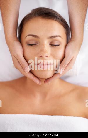 Den richtigen Kopfraum zu finden. Blick aus der Vogelperspektive auf eine junge Frau, die in einem Spa liegt und eine Kopfmassage erhält. Stockfoto