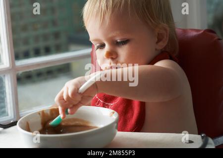 Wachsender Junge braucht sein Essen. Ein kleiner Junge, der in seinem Hochstuhl nach Herzenslust isst. Stockfoto