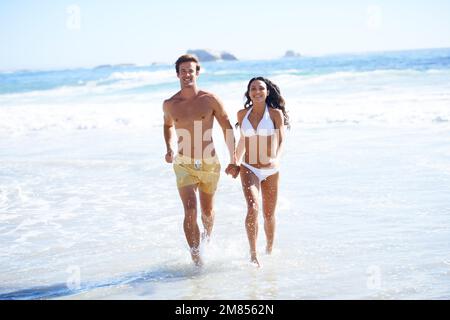 Ich genieße die Sonne. Ein glückliches Paar in Badebekleidung, das zusammen am Strand läuft. Stockfoto