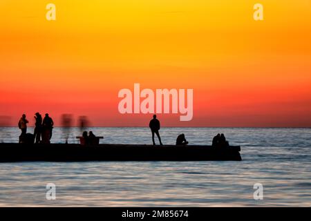 Silhouette von Menschen, die den Sonnenuntergang auf dem Molo Audace im alten Hafen von Triest, Italien, beobachten Stockfoto