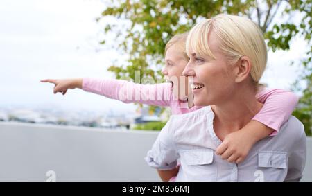 Sieh Mal, Mom. Ein junges Mädchen, das zur Seite zeigt, während es auf dem Rücken seiner Mutter sitzt. Stockfoto