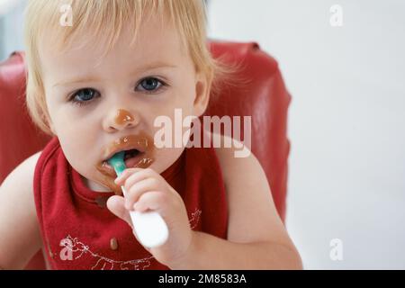 Wachsender Junge braucht sein Essen. Ein kleiner Junge, der in seinem Hochstuhl nach Herzenslust isst. Stockfoto