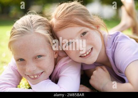 Schwestern und beste Freunde. Zwei kleine Mädchen, die glücklich auf dem Rasen liegen. Stockfoto