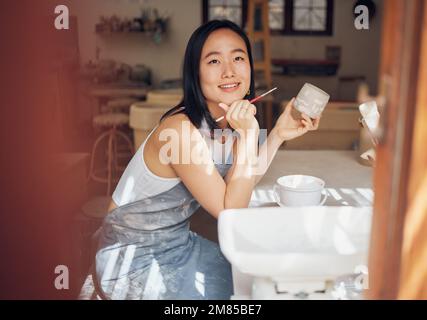 Asiatische Frau, Töpferei und Denken beim Malen in Werkstatt, Kreativstudio und Design-Startup. Glückliche Malerin, Tonkeramik und Pinselideen Stockfoto