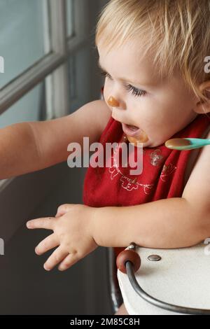 Wachsender Junge braucht sein Essen. Ein kleiner Junge, der in seinem Hochstuhl nach Herzenslust isst. Stockfoto