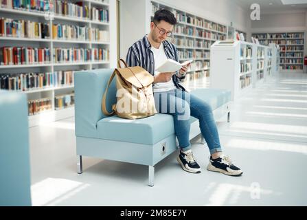 Bibliothek, Lesen und Mann mit Buch auf dem Sofa für Bildung, Studium und akademische Forschung. Universität, Stipendium und männlicher Student auf der Couch Stockfoto