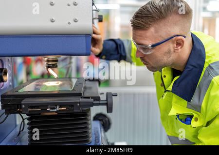 Ingenieur sitzt im Roboterfabrikationsraum und verwendet das Messmikroskop Maschinenprüfung Mikrochip Stockfoto