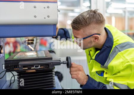 Ingenieur sitzt im Roboterfabrikationsraum und verwendet das Messmikroskop Maschinenprüfung Mikrochip Stockfoto