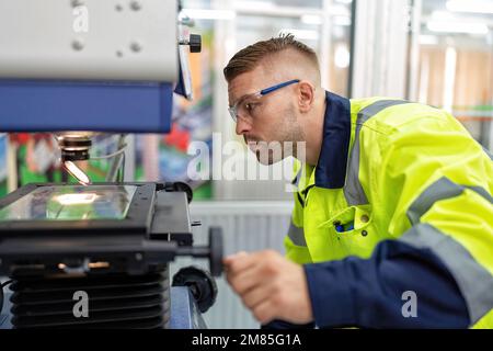 Ingenieur sitzt im Roboterfabrikationsraum und verwendet das Messmikroskop Maschinenprüfung Mikrochip Stockfoto