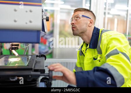 Ingenieur sitzt im Roboterfabrikationsraum und verwendet das Messmikroskop Maschinenprüfung Mikrochip Stockfoto