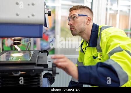 Ingenieur sitzt im Roboterfabrikationsraum und verwendet das Messmikroskop Maschinenprüfung Mikrochip Stockfoto