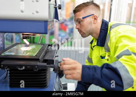 Ingenieur sitzt im Roboterfabrikationsraum und verwendet das Messmikroskop Maschinenprüfung Mikrochip Stockfoto