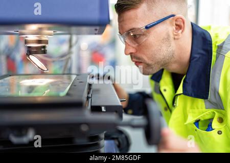 Ingenieur sitzt im Roboterfabrikationsraum und verwendet das Messmikroskop Maschinenprüfung Mikrochip Stockfoto