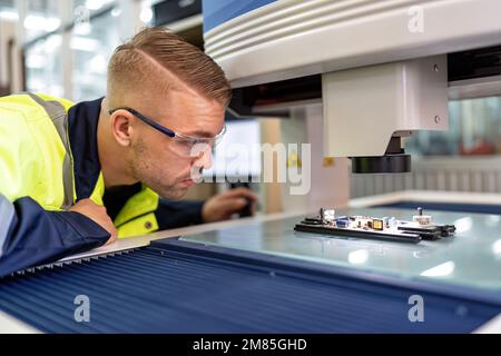 Techniker, der im Roboterherstellungsraum sitzt, verwenden das Messmikroskop, um die elektronische Platine zu prüfen Stockfoto