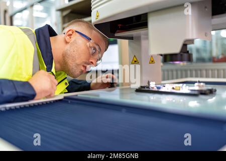 Techniker, der im Roboterherstellungsraum sitzt, verwenden das Messmikroskop, um die elektronische Platine zu prüfen Stockfoto