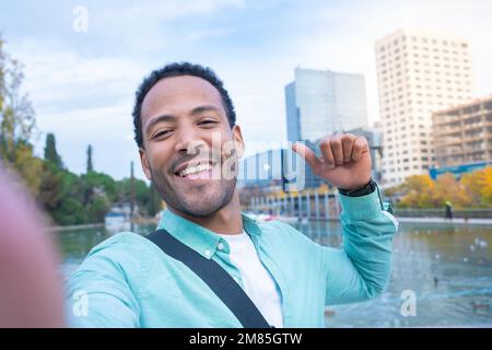 Ein junger afroamerikanischer Mann, der ein Selfie macht, in die Kamera schaut und lächelt - Touristenstudent Stockfoto