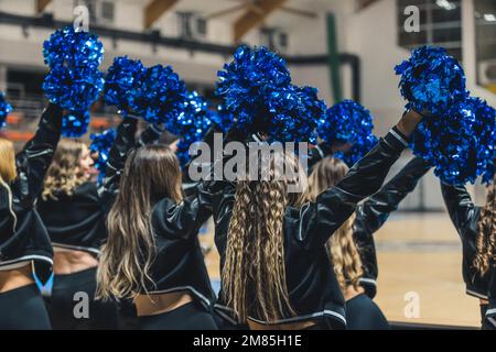 Eine Gruppe von Cheerleader wird mitten in der Performance gefangen, ihre blauen Pom-Poms winken in der Luft, während sie ihr Team während eines Spiels anfeuern. Die jungen Frauen sind voller Energie und Aufregung. Stockfoto