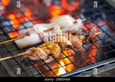 Ein paar Spieße Schweinebauch werden unter einem starken Kohlefeuer gegrillt Stockfoto