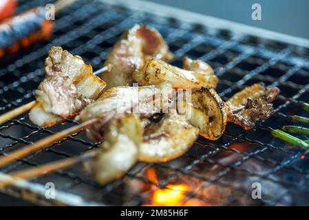 Ein paar Spieße Schweinebauch werden unter einem starken Kohlefeuer gegrillt Stockfoto