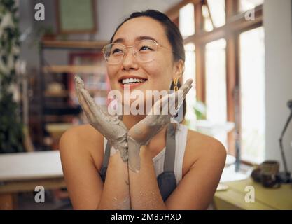 Hände, Gesicht und schmutzig mit einer asiatischen Töpferin, die in ihrem Atelier oder ihrer Werkstatt sitzt. Kunst, Design und Kreativität mit einer Designerin oder Stockfoto