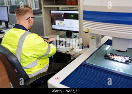 Techniker, der im Roboterherstellungsraum sitzt, verwenden das Messmikroskop, um die elektronische Platine zu prüfen Stockfoto