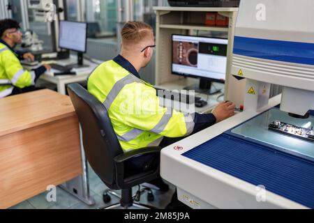 Techniker, der im Roboterherstellungsraum sitzt, verwenden das Messmikroskop, um die elektronische Platine zu prüfen Stockfoto