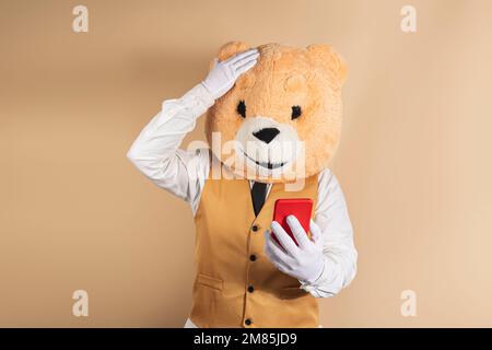 Aufgeregter Mann in Bärenmaske, der gute Nachrichten auf dem Handy auf gelbem Hintergrund liest. Stockfoto