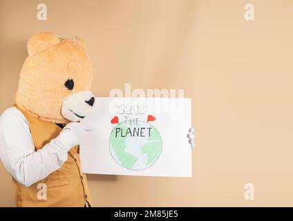 Ein Mann mit einer Teddybärmaske auf gelbem Hintergrund hält ein Schild mit der Aufschrift: "Rette den Planeten." Speicherplatz kopieren. Planet Care-Konzept Stockfoto