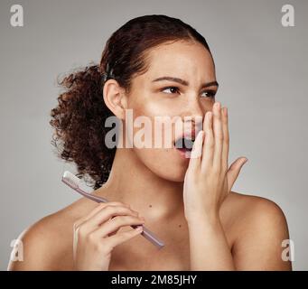 Zahnbürste, Frau und Mundgeruch mit Zahnproblemen, während der Geruch nach Mund, Zähnen oder Zahnfleisch in der Hand riecht. Gesicht einer Frau im Mundgesundheitsstudio Stockfoto