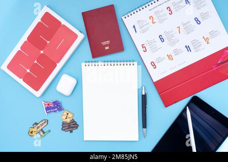 Konzept für Urlaub, Reise oder Urlaubsplanung in Neuseeland – Feiertagskalender mit Notizblock, Stift, Kopfhörer und Tablet auf blauem Hintergrund. Stockfoto