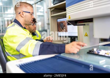 Techniker, der im Roboterherstellungsraum sitzt, verwenden das Messmikroskop, um die elektronische Platine zu prüfen Stockfoto