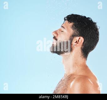 Wasser, Reinigung und Gesicht mit Mann und Schönheit, Dusche für Hygiene und Pflege mit Hautpflege vor blauem Studiohintergrund. Reinigen Sie das Profil mit Stockfoto