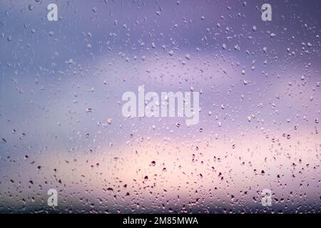 Natürliche Wassertropfen an einem Fenster stellen sich dem Sonnenuntergang entgegen. Stockfoto