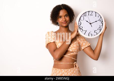 Ein hübsches Mädchen, das einen Countdown macht, mit einer großen Uhr auf einem isolierten weißen Hintergrund. Stockfoto